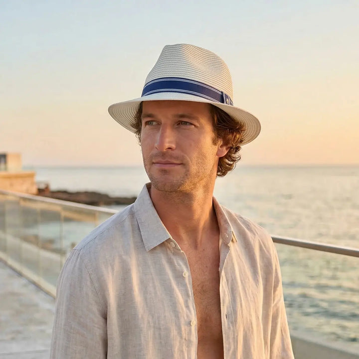 Man wearing a Stripe Fedora sun hat with a blue band by the sea at sunset